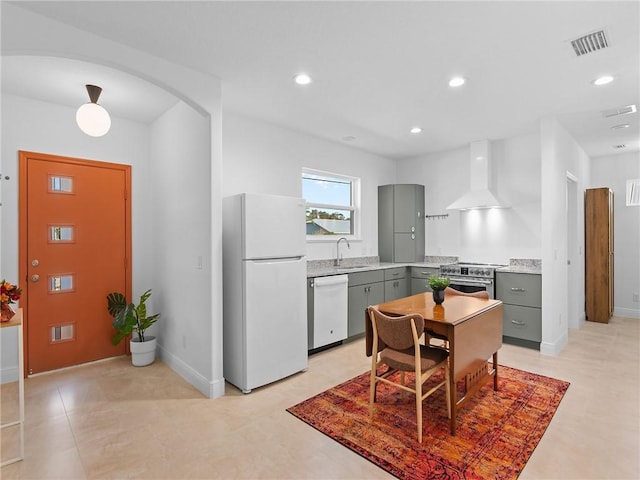 kitchen with stainless steel stove, dishwasher, white fridge, wall chimney range hood, and gray cabinetry