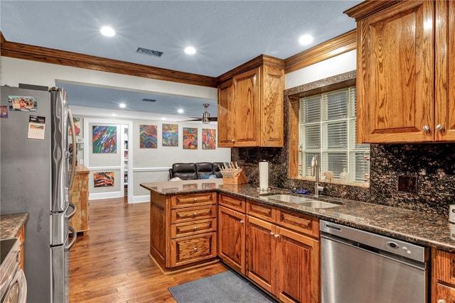 kitchen featuring light hardwood / wood-style floors, sink, kitchen peninsula, appliances with stainless steel finishes, and dark stone counters