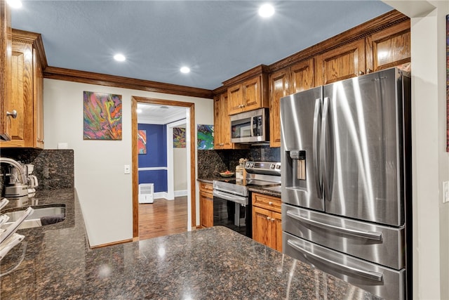 kitchen featuring ornamental molding, appliances with stainless steel finishes, decorative backsplash, sink, and dark stone countertops