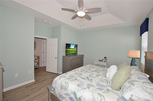 bedroom with wood finished floors, a raised ceiling, a ceiling fan, and baseboards