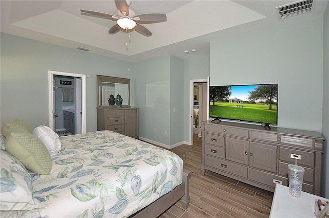 bedroom with wood finished floors, a raised ceiling, visible vents, and baseboards