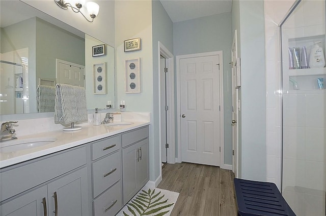 bathroom featuring double vanity, a stall shower, a sink, and wood finished floors