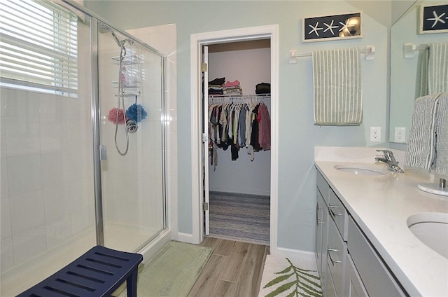 bathroom with double vanity, a shower stall, a sink, and wood finished floors