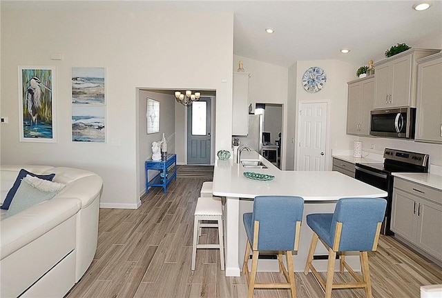 kitchen featuring stainless steel microwave, a breakfast bar area, wood tiled floor, a sink, and range with electric stovetop