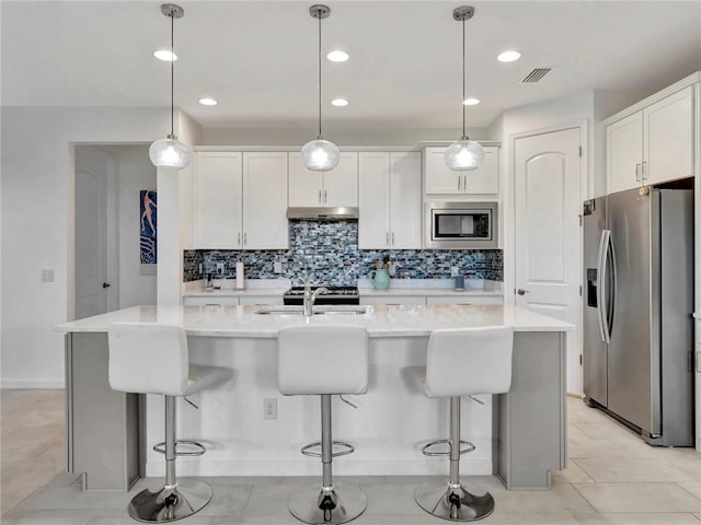 5205 Turtle Creek Cir, Vero Beach, FL 32967 - kitchen featuring stainless steel appliances, under cabinet range hood, decorative backsplash, white cabinetry, and a breakfast bar