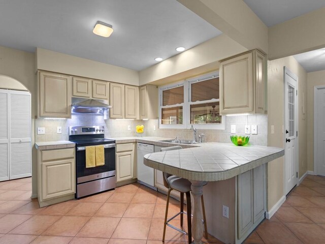 2237 10th Ave, Vero Beach, FL 32960 - kitchen featuring under cabinet range hood, tile countertops, a sink, white dishwasher, and stainless steel electric range