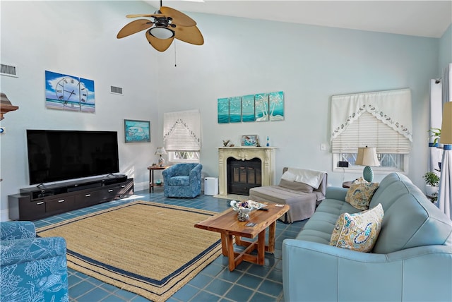 living room with ceiling fan, a towering ceiling, and a fireplace