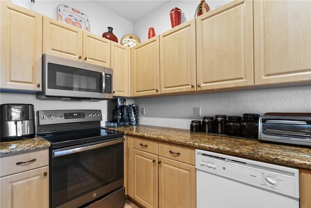 kitchen featuring stainless steel appliances, dark stone counters, and light brown cabinetry