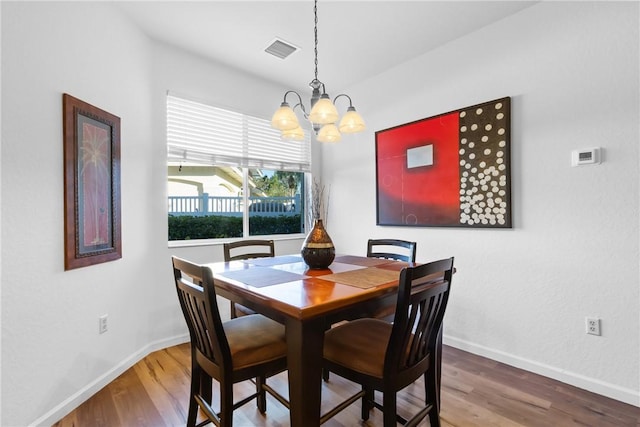 dining space with an inviting chandelier, wood finished floors, visible vents, and baseboards