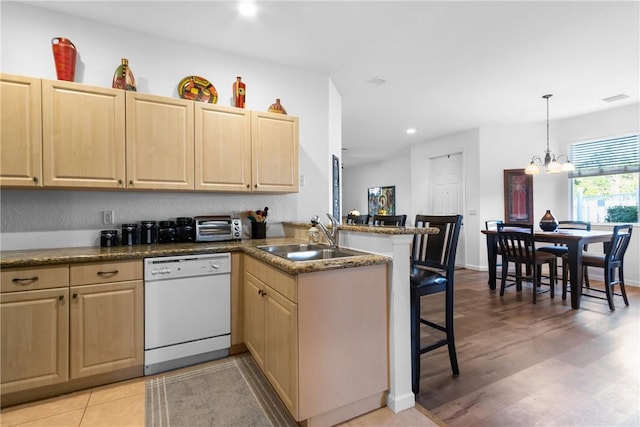 kitchen featuring a breakfast bar area, a peninsula, a sink, dishwasher, and light brown cabinetry