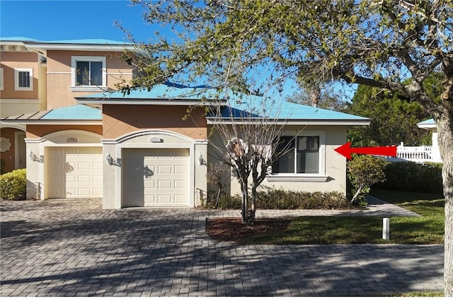 view of front facade featuring a garage, fence, decorative driveway, and stucco siding