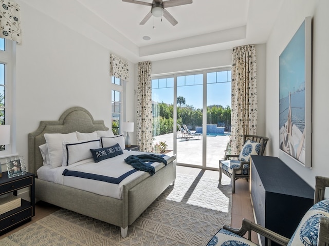 bedroom with access to exterior, hardwood / wood-style flooring, a raised ceiling, and ceiling fan