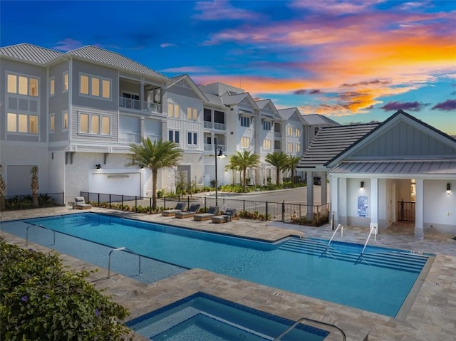 pool at dusk featuring a hot tub