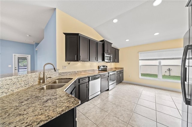 kitchen with appliances with stainless steel finishes, a sink, lofted ceiling, light stone countertops, and a peninsula