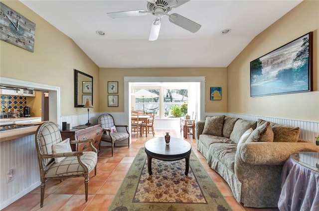 living area with a ceiling fan, lofted ceiling, a wainscoted wall, and light tile patterned floors