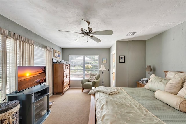 bedroom with light carpet, a textured ceiling, visible vents, and a ceiling fan