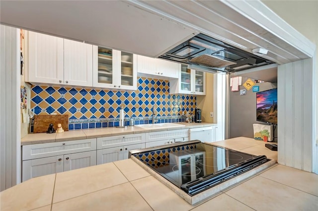 kitchen with black electric cooktop, a sink, white cabinets, decorative backsplash, and glass insert cabinets