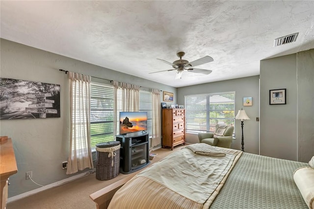 bedroom featuring ceiling fan, a textured ceiling, light colored carpet, visible vents, and baseboards