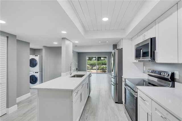 kitchen featuring stacked washing maching and dryer, baseboards, a sink, light countertops, and stainless steel appliances