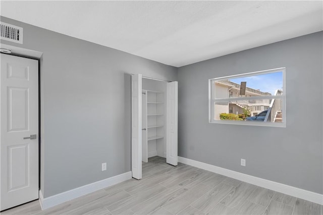 unfurnished bedroom with baseboards, wood tiled floor, a closet, and visible vents