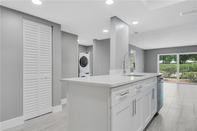 kitchen with stacked washer / dryer, an island with sink, light countertops, white cabinets, and a sink