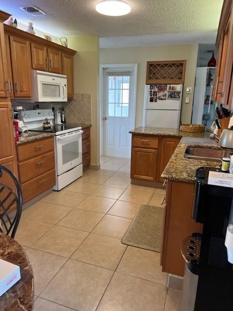 kitchen with white appliances, a sink, brown cabinets, a textured ceiling, and dark stone countertops