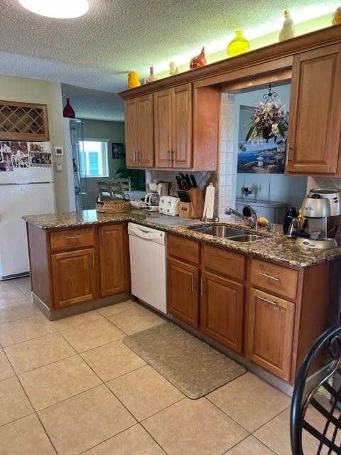 kitchen with white appliances, a sink, brown cabinetry, a peninsula, and a textured ceiling