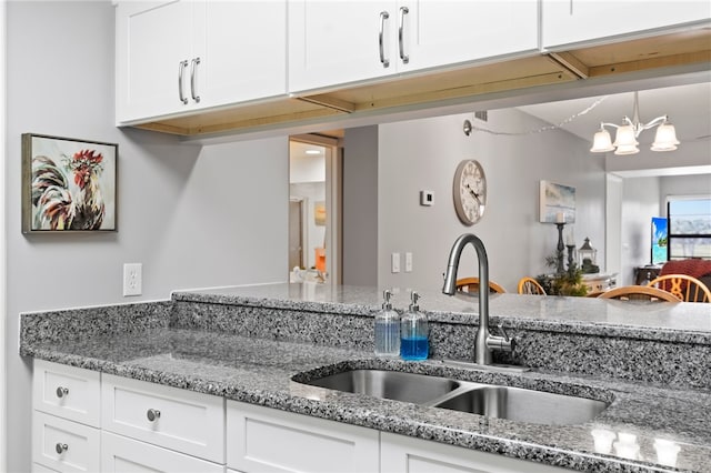 kitchen with white cabinetry, pendant lighting, light stone countertops, sink, and a chandelier