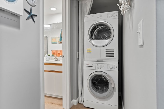 clothes washing area featuring stacked washing maching and dryer, sink, and light hardwood / wood-style flooring