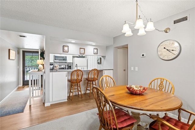 dining area featuring a chandelier, a textured ceiling, and light hardwood / wood-style flooring