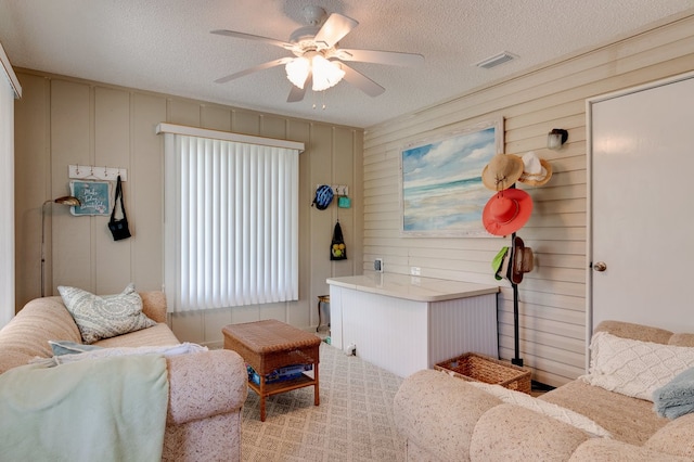 living room with a textured ceiling, ceiling fan, and wooden walls