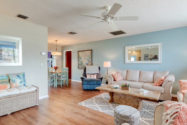 living room with ceiling fan, a textured ceiling, and light wood-type flooring