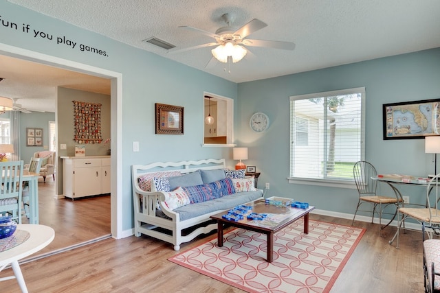 living room with ceiling fan, light hardwood / wood-style floors, and a textured ceiling