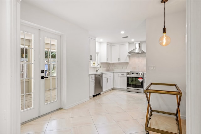 kitchen featuring stainless steel appliances, backsplash, pendant lighting, white cabinets, and wall chimney exhaust hood