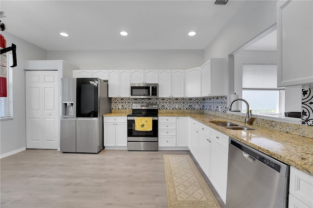 kitchen with white cabinetry, appliances with stainless steel finishes, sink, and light stone counters