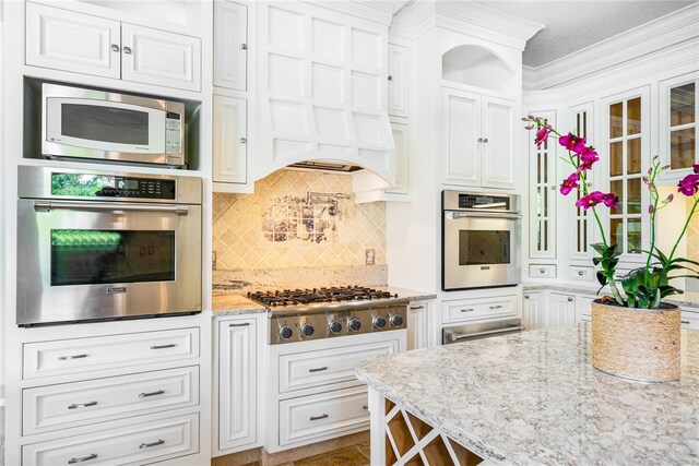 kitchen with white cabinetry, appliances with stainless steel finishes, light stone counters, and crown molding