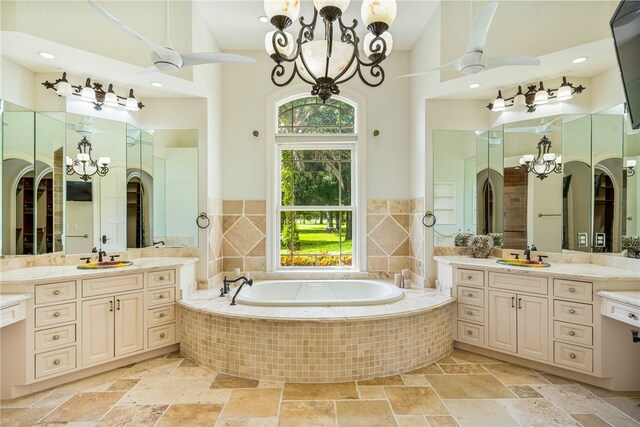 bathroom featuring vanity, tiled bath, and ceiling fan with notable chandelier