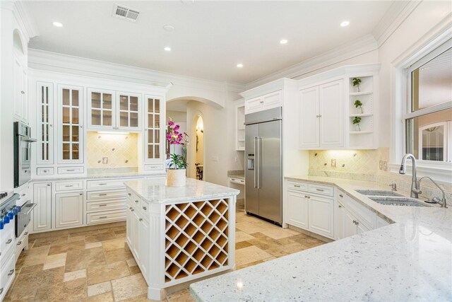 kitchen with stainless steel appliances, sink, light stone counters, white cabinets, and decorative backsplash