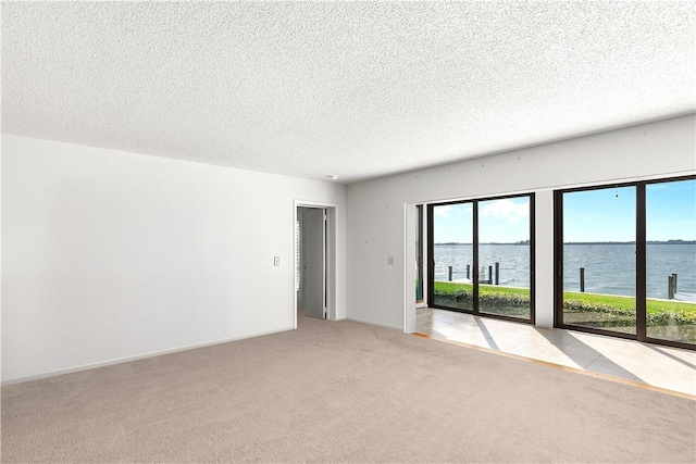 spare room featuring baseboards, a water view, light carpet, and a textured ceiling