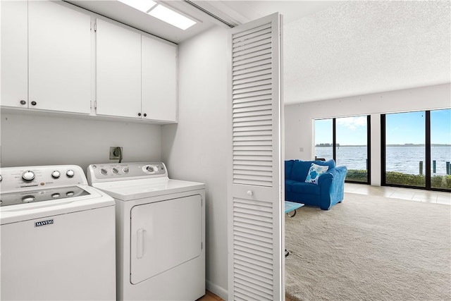 washroom featuring cabinet space, light colored carpet, a water view, a textured ceiling, and separate washer and dryer