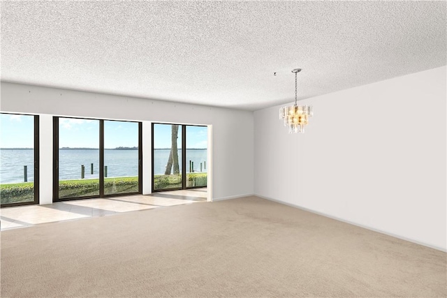 empty room featuring a water view, a chandelier, a textured ceiling, and light colored carpet