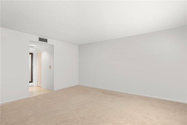 unfurnished room featuring visible vents, light colored carpet, a textured ceiling, and baseboards