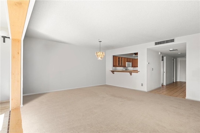 unfurnished living room with a textured ceiling, light colored carpet, visible vents, baseboards, and an inviting chandelier