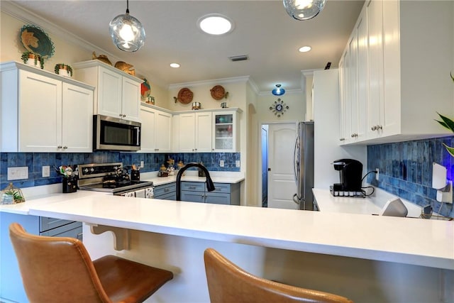 kitchen featuring decorative light fixtures, white cabinets, a kitchen bar, kitchen peninsula, and stainless steel appliances