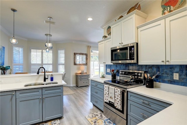 kitchen featuring appliances with stainless steel finishes, decorative light fixtures, white cabinetry, sink, and ornamental molding