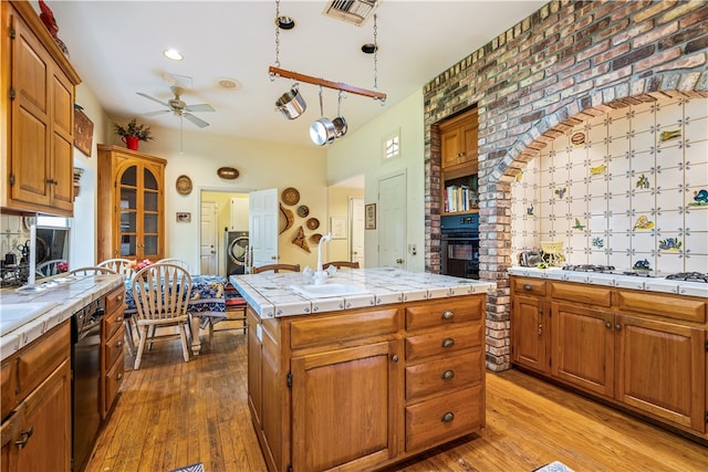 kitchen featuring tile countertops, light hardwood / wood-style floors, black appliances, decorative light fixtures, and a center island