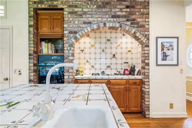 bar featuring tile countertops, gas cooktop, black oven, and hardwood / wood-style flooring