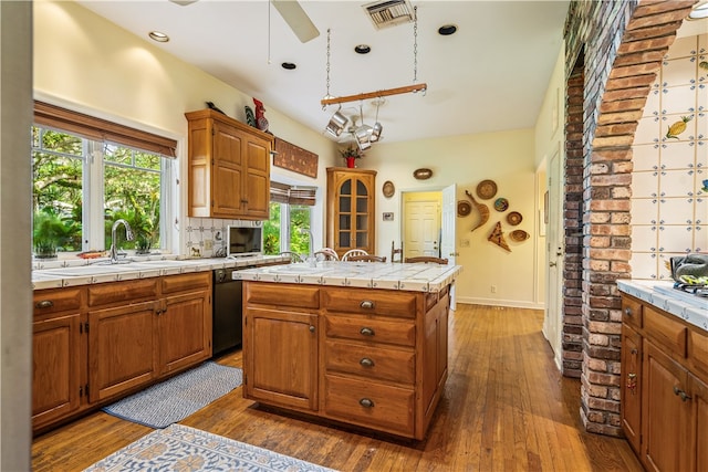 kitchen featuring tile countertops, black dishwasher, sink, dark hardwood / wood-style floors, and a kitchen island