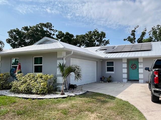 view of front of home with stucco siding, roof mounted solar panels, concrete driveway, an attached garage, and metal roof