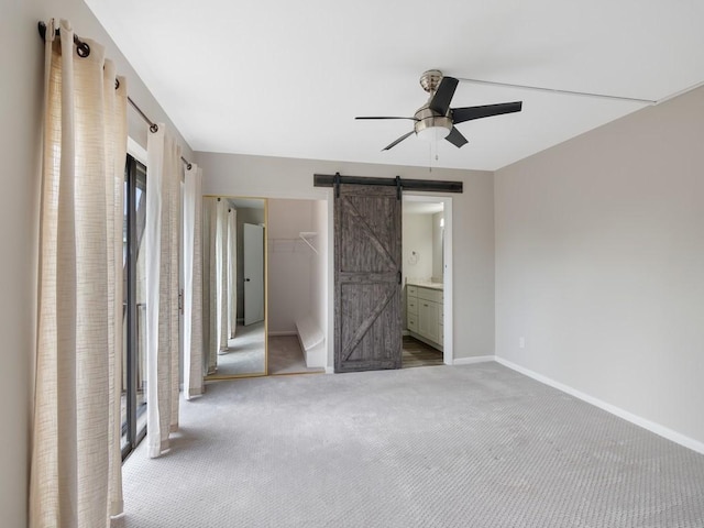 unfurnished bedroom with ceiling fan, connected bathroom, carpet floors, a barn door, and a closet